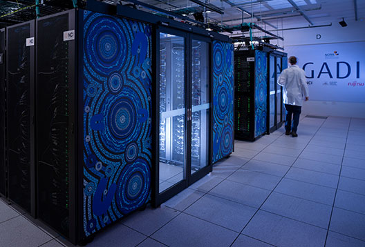 Servers in a supercomputer lit blue in a dim room, with blue Aboriginal style dot artwork