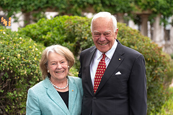 A woman and man stand in front of a garden smiling for the camera.